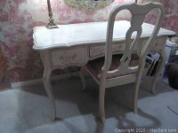 Desk and chair set in front of wallpapered wall with mirror and lamps