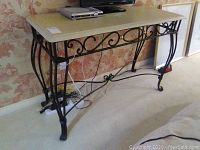 Full view of Bombay Company wrought iron console table with cream resin top by wall with electronics on top.