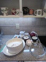 Overall countertop view showing various ceramic dishes including pitcher, mugs, egg dishes, quiche dishes, and pie plates.