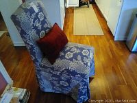 Armless slipper chair in blue and white floral Larissa Jacquard Stripe upholstery with a red rectangular pillow. Shows overall wear and the front edge of the seat fabric worn through.