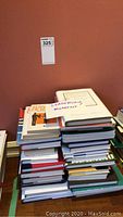 Stack of 35 books on leadership, management, and coaching topics stacked against a brown wall with an auction sticker number 325 above