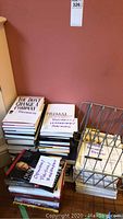 Stack of business and leadership books with visible titles such as 'You Don't Change a Dying Company', 'Primal Business Leadership Coaching', and others on opinions, politics, biography. Includes a metal rack and marked papers.