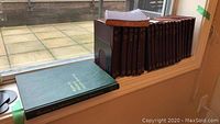 Photo of 15 burgundy hardcover business books and 1 green hardcover binder placed on window sill