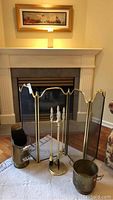 Full view of the brass fire screen in front of a stone fireplace with fire tools, coal scuttle and pot arranged on a white mat.