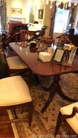 Full view of the Duncan Phyfe style wooden dining table with surrounding dining chairs and decorative items on top.
