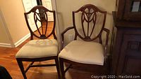 Two dining chairs with shield back design and beige striped upholstery shown from front, one with arms and one without.