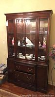 Front view of the wood china cabinet showing three glass front doors with displayed items inside and the lower section with drawers and cabinets.