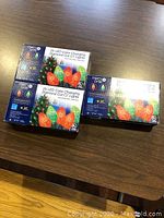 Photo showing three boxed sets of 25 LED color changing diamond cut C7 lights on a wooden table. The boxes are blue with images of red and green lights and the MerryBrite brand name visible.