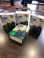 Four unopened boxes of multi-color 50 LED dome holiday lights on a table.