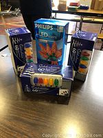 Four boxed sets of string lights on a table. Three boxes contain 60 LED multi-color lights labeled Celebrations, and one box contains 60 LED red lights labeled Philips.