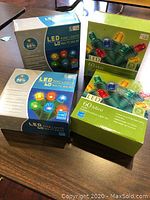 Four boxed sets of 60 mini multi-color LED string lights sitting on a table. Two boxes measure 16 feet in length and the other two are 15 feet each. Boxes show energy saving feature and LED bulbs in red, blue, green, and yellow colors.