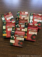 Seven boxes of Ultra LED battery operated wreath lights, four white light boxes and three multi-color light boxes, arranged on a wooden surface.