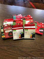 Nine unopened boxes of battery operated LED string lights clustered on a table, predominantly red packaging with product branding and images of LED bulbs and wreath placement.