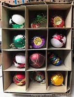 Photo of 12 vintage Christmas tree ornaments in divided cardboard box showing a variety of colors and glittery designs.
