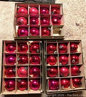 Three cardboard boxes containing a total of 35 large red and pink shiny spherical Christmas ornaments.