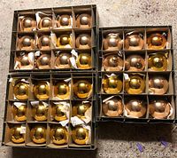 Photo showing 36 large vintage gold Christmas ornaments in two open cardboard trays, some missing hooks and tops.