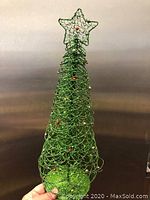 Photo showing the green wire Christmas tree with star topper and red ornaments against a plain background.