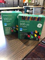 Two boxes of Energy Smart 100 LED C-5 lights with GE logo, displayed on wood table in room.