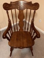 Full view of solid oak rocking chair showing its wooden frame, spindled back, armrests, and rockers on the base.