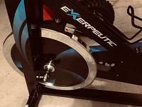 Close-up view of the Exerpeutic bike's flywheel and frame showing the logo and blue accents, highlighting its sturdy build.