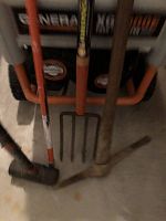 Photo showing pitchfork, pick axe, and sledgehammer leaning against a surface with a generator in background.