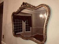 Full view of the gold framed wall mirror hanging on a wall, showing its ornate curved shape and reflection of the room.