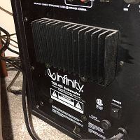 Rear side close-up showing the heat sink, power switch, speaker terminals, fuse holder, and Infinity branding on the TSS-450 subwoofer.