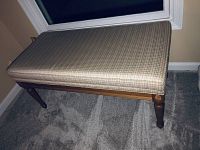 Window bench with a plaid upholstered top, showing wooden legs and frame from the front angle.