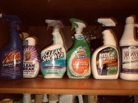 Seven bottles of household cleaning products arranged on a shelf. Includes spray bottles and a bottle with a cap shown front facing.