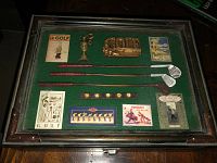 Top down view of vintage golf accessory box showing contents including miniature clubs, ball markers, pins and cards on green felt.