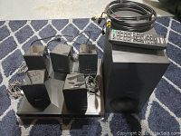 Photo of main unit, five small speakers, subwoofer, remote control, and cables arranged on carpeted floor.