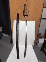 Full view of the samurai sword standing on a chair with the wooden scabbard beside it showing overall size and form.