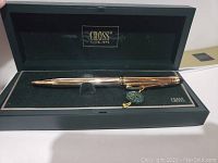 Close-up view of the Cross 10 KT Gold Filled ballpoint pen in the black velvet-lined gift box, showing side profile and detailing, including hanging tag.