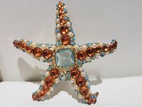 Front close-up of vintage KJL starfish brooch with amber cabochons, pearls, blue beads and blue gem center