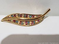 Front view of the gold-tone leaf shaped brooch featuring multicolored rhinestones and faux pearls.