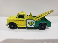 Side view showing yellow cab with black wheels and green flatbed tow truck with BP logos on door panels, showing paint wear and chips on the front and sides.