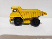 Side view of yellow Hot Wheels dump truck toy showing metal body and rubber tires