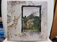 Front cover of vinyl record showing a man carrying sticks framed by peeling wallpaper effect with signs of wear and peeling on edges.