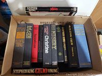 Photo showing the box with 12 Stephen King books stacked, titles visible include Misery (paperback), Needful Things, The Dark Half, Salem's Lot, Christine, Misery (hardcover), Skeleton Crew, Carrie, and Nightmares & Dreamscapes.