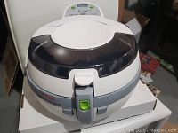 Front view of the white T-Fal Actifry Original hot air fryer showing the transparent tinted lid, handle with green button, and control panel.