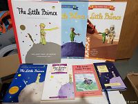 Seven Little Prince books displayed, including three larger books and four smaller ones. The deluxe pop-up book is prominent with its white cover and red spine.