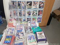 Binder sleeves filled with baseball cards displayed upright along with loose cards in bags and boxes on table.