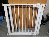 Frontal view of one white metal Safety 1st adjustable safety gate showing vertical bars, hinged locking door with locking indicator on top right and width adjustment screws on each side.