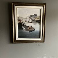 Full view of the framed oil painting showing boats docked by a pier and houses in the background with calm water reflections.