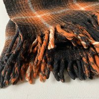 Close-up of wool blanket's twisted fringe in orange, black, and cream colors.