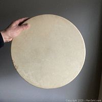 Front view of the drum showing smooth natural deer skin stretched over wood frame, held by hand to illustrate size.