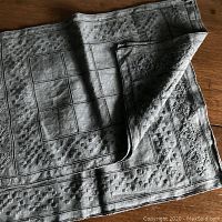 Full view of folded placemat showing hand dyed blue gray color and textured embroidery pattern