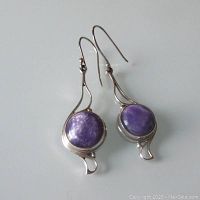 Pair of Art Nouveau style sterling silver earrings with round purple charoite cabochon stones and curved decorative silver accents on fishhook ear wires.