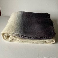 Folded dip dyed wool throw showing gradient from cream to dark grey with hand-fringed edges.