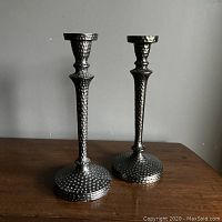Pair of black bronze-colored metal candle sticks with hammered texture, standing on a wooden surface.